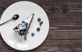 Piece of homemade bird cherry cake with sour cream, decorated with blueberries and mint leaves on a white plate. dark wooden Royalty Free Stock Photo