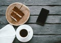 Piece of a homemade biscuit cake and black coffee on a black wooden table. Smartphone on a table