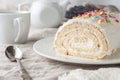 A piece of homemade biscuit roll with butter cream. Decorated with colorful topping. On a white plate. In the background is a Royalty Free Stock Photo