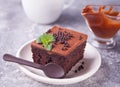 A piece of homemade chocolate cake on the plate with icing, mint leaf and chocolate spoon on the gray table Royalty Free Stock Photo