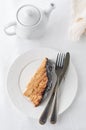 A piece of homemade multi-layer biscuit cake. Soaked in butter cream. Garnished with chocolate icing and coconut. On a white plate