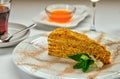 Piece of honey cake and fresh mint on white plate. Served with a rosette of honey, a cup of aromatic tea and a glass of white wine Royalty Free Stock Photo