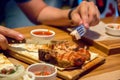 A piece of kebab, on a wooden plate, men`s hands holding a fork and a knife