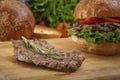 Piece of meat fried on the grill with a sprig of rosemary lies on a wooden board for a burger on a background of greens Royalty Free Stock Photo