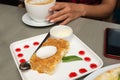 A piece of Napoleon cake decorated with drops of jam and the hands of a girl holding coffee, slice of pie with ice cream and the h