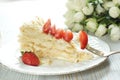 A piece of Napoleon cake on a plate adorned with a red ripe strawberry, a fork with a stuck piece of dessert Royalty Free Stock Photo