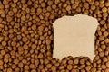 A piece of paper with torn edges lies on top of dog food. Brown pellets of dry pet food. An empty piece of paper. Pet food. Copy