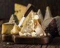 Piece of Parmesan cheese on the wooden board. Assortment of different cheeses at the background