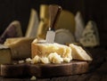 Piece of Parmesan cheese on the wooden board. Assortment of different cheeses at the background