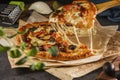 A piece of pizza with bacon, basil, olives, pickles and mozzarella cheese close-up on parchment paper on a dark background. Royalty Free Stock Photo