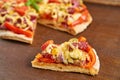 Piece of pizza isolated with salami, tomatoes, bell pepper, onion, green olives, corn, cheese and spices on brown wooden table Royalty Free Stock Photo