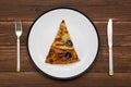 A piece of pizza on white plate with a knife and fork on wooden background. Slice of tasty pizza on the plate. Top view Royalty Free Stock Photo