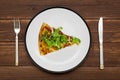 A piece of pizza on white plate with a knife and fork on wooden background. Top view Royalty Free Stock Photo