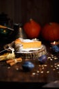 Piece of pumpkin cheesecake with powdered sugar, plums, pumpkins, table lamp on a dark wooden background Royalty Free Stock Photo