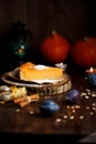 Piece of pumpkin cheesecake with powdered sugar, pumpkins, table lamp on a dark wooden background