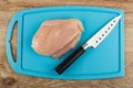 Piece of raw chicken fillet, knife on cutting board on wooden table. Top view Royalty Free Stock Photo