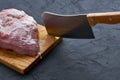 a piece of raw meat and a knife stuck on a cutting board on a dark background