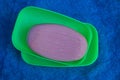 A piece of red soap in a plastic green soap dish on blue matter Royalty Free Stock Photo