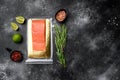 Piece of salmon fillets in a vacuum blister pack, with herbs, on black dark stone table background, top view flat lay, with copy