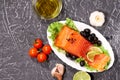 A piece of salmon on a white plate with olives and lemon, on a gray background. Selective focus