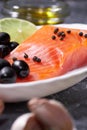 A piece of salmon on a white plate with olives and lemon, on a gray background. Selective focus