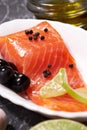 A piece of salmon on a white plate with olives and lemon, on a gray background. Selective focus