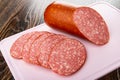 Piece of sausage, slices of cervelat on pink cutting board on wooden table Royalty Free Stock Photo