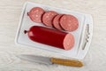Piece of sausage, slices of sausage on cutting board, knife on wooden table. Top view Royalty Free Stock Photo