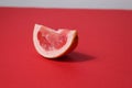 A piece of a slice of red grapefruit on a red background with a hard shadow. Fruit creative benefit red on red Royalty Free Stock Photo