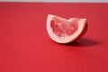 A piece of a slice of red grapefruit on a red background with a hard shadow. Fruit creative benefit red on red Royalty Free Stock Photo