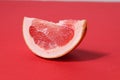 A piece of a slice of red grapefruit on a red background with a hard shadow. Fruit creative benefit red on red Royalty Free Stock Photo