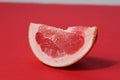 A piece of a slice of red grapefruit on a red background with a hard shadow. Fruit creative benefit red on red Royalty Free Stock Photo