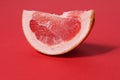 A piece of a slice of red grapefruit on a red background with a hard shadow. Fruit creative benefit red on red Royalty Free Stock Photo