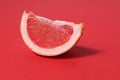 A piece of a slice of red grapefruit on a red background with a hard shadow. Fruit creative benefit red on red Royalty Free Stock Photo