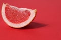 A piece of a slice of red grapefruit on a red background with a hard shadow. Fruit creative benefit red on red Royalty Free Stock Photo