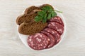 Piece and slices of smoked sausage, parsley, slices of bread in plate on wooden table. Top view Royalty Free Stock Photo