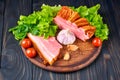 Piece of smoked pork belly with sliced strip and grain bread on a wooden cutting board. Vegetables: tomatoes, lettuce, parsley,