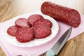 Piece of smoked sausage, slices of sausage in plate on cutting board, knife on wooden table Royalty Free Stock Photo