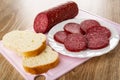 Piece of smoked sausage, slices of sausage in plate, slices of bread on cutting board on wooden table Royalty Free Stock Photo