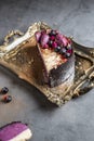 Piece of the tasty cake decorated with fruit on a gold tray costs on a gray background