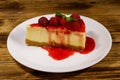 Piece of tasty New York cheesecake with raspberries and raspberry jam in a white plate on wooden table