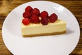 Piece of tasty New York cheesecake with raspberries in a white plate on wooden table