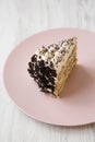 A piece of tiramisu cake on a pink plate on a white wooden surface, side view. Close-up