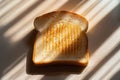 A piece of toasted white bread in the shadow on the table. A slice of bread on a beige table Royalty Free Stock Photo