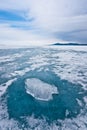 A piece of transparent ice on a circle of transparent blue ice on the ice of baikal, mountains in the distance and the sky