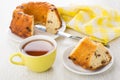 Piece of Viennese cake in plate, yellow napkin, cup of tea