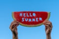 A piece of watermelon against a blue sky. Children`s hands are holding a slice of watermelon with the text Hello Summer. Summer Royalty Free Stock Photo