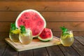 Piece of watermelon, half of watermelon and glasses of refreshing summer lemonade on rustic wooden table