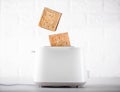 a piece of wheat bread in a toaster. fried toast flies of a white toaster on a white background