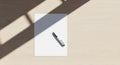 A piece of white paper with a pen rests on a light wood surface. Sunlight creates Royalty Free Stock Photo